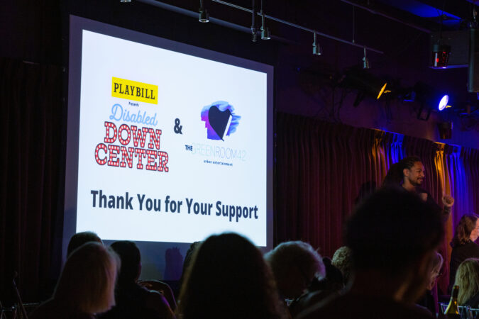 A screen that says: thank you for your support with the logo for DISABLED DOWN CENTER and the GREEN ROOM 42 above that ext on a large projector screen. A sold out audience looks on.